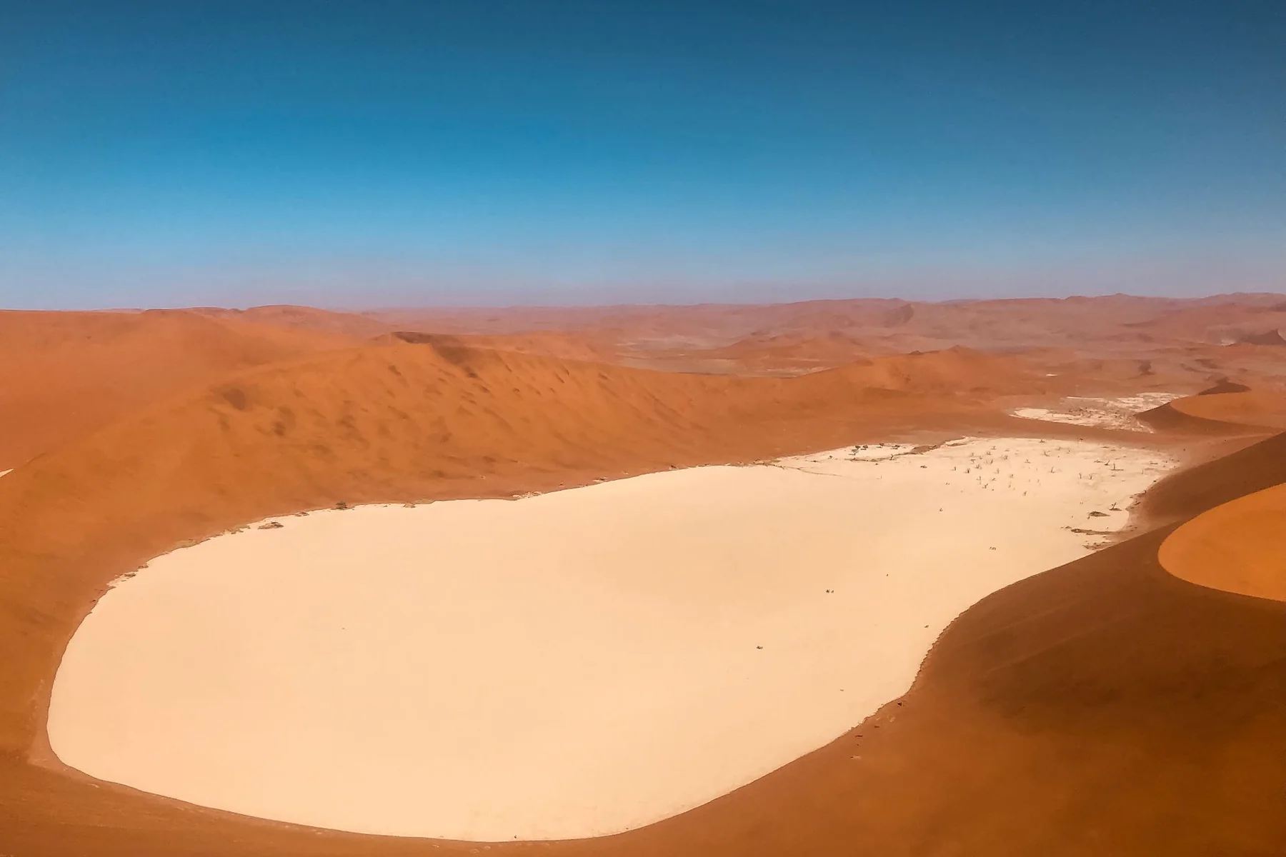 Red dunes curving around a white clay pan in the Namib Desert, Namibia
