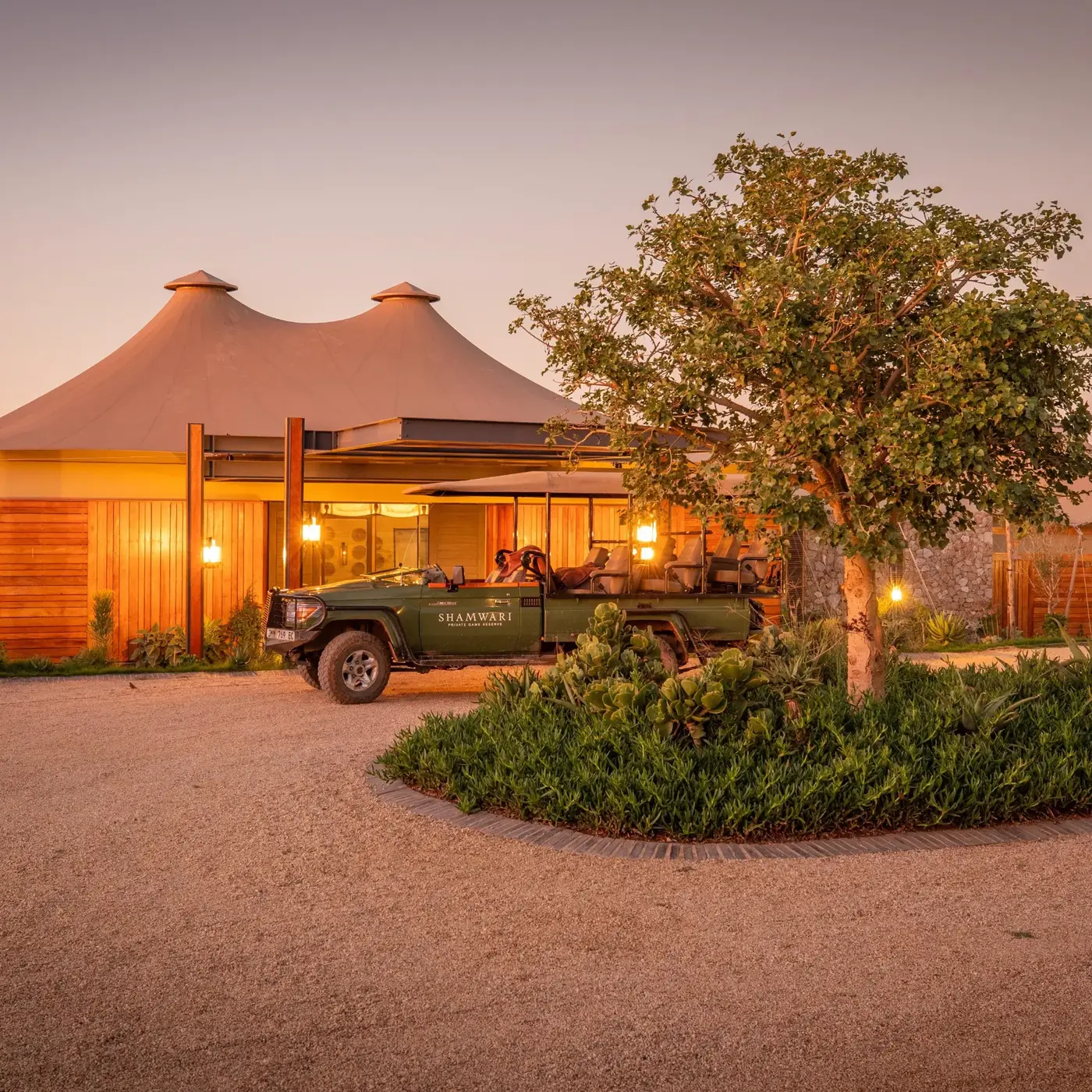 Owner-run safari lodge at dusk with a game-drive vehicle waiting at the entrance