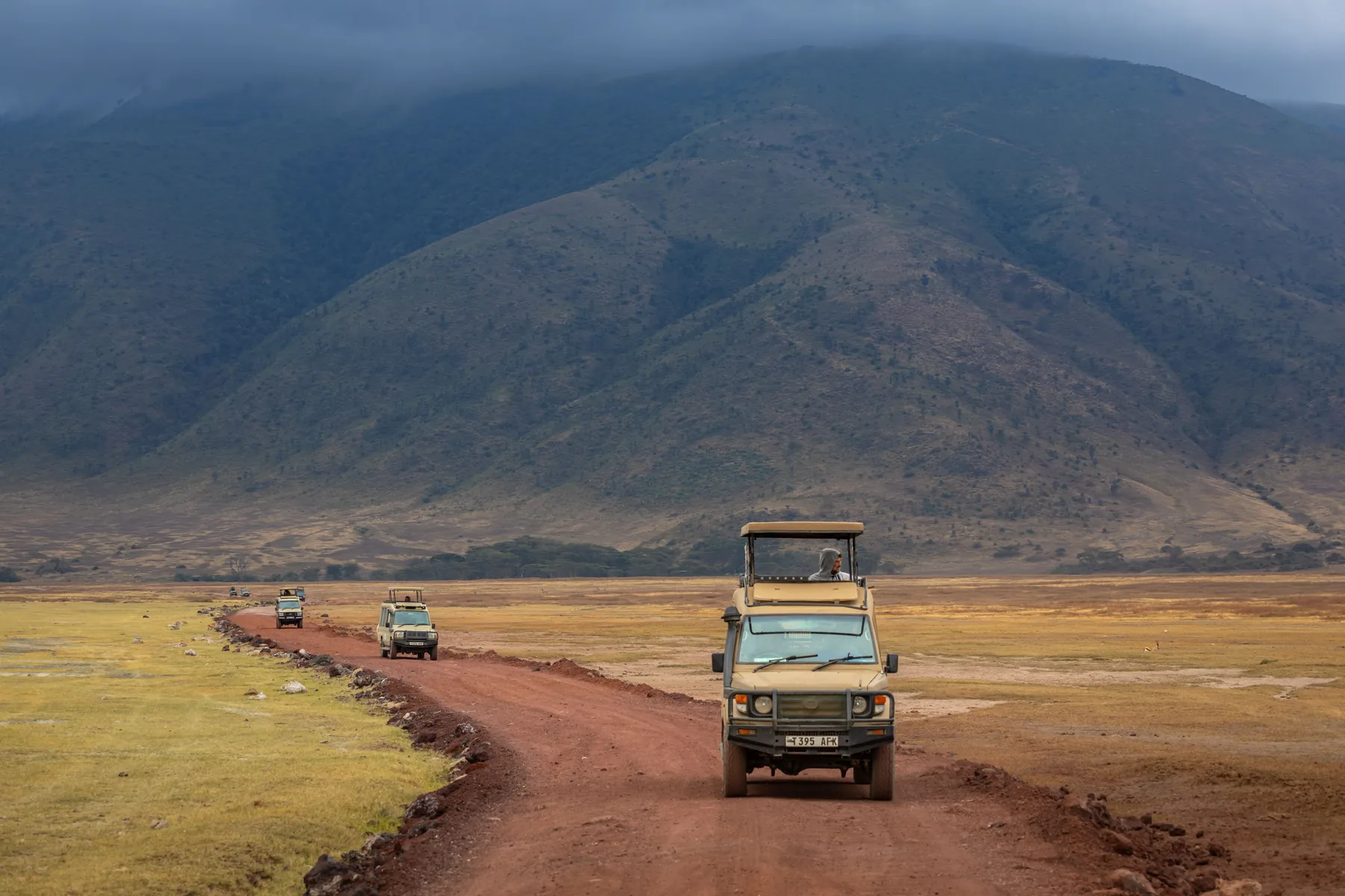 Safari vehicles descending the red dirt road into the Ngorongoro Crater