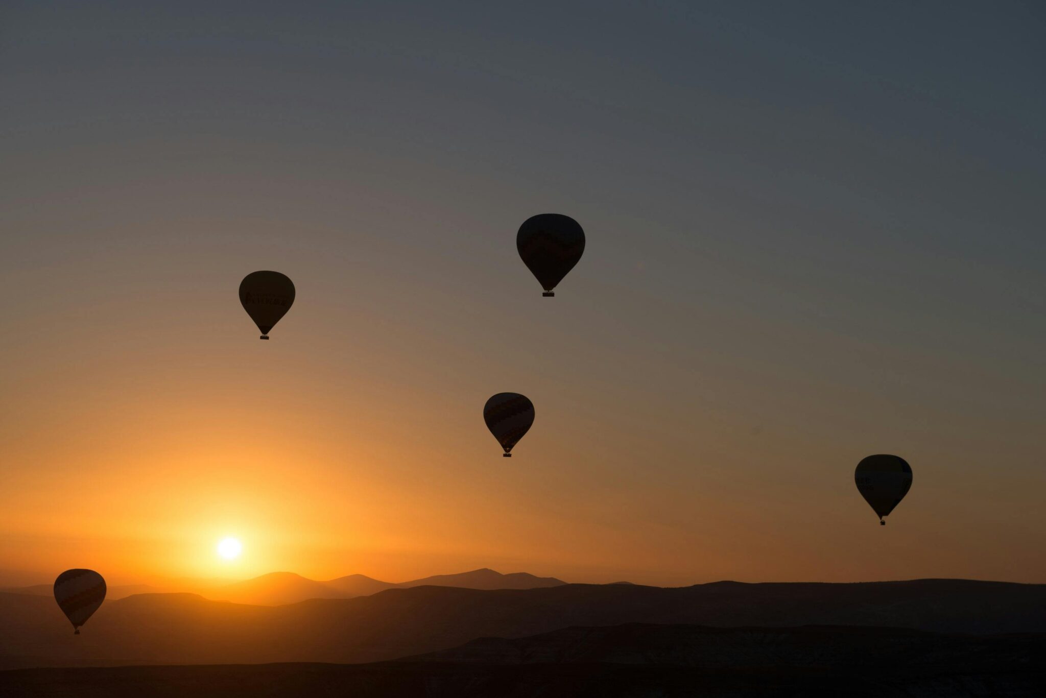 Silhouetted hot air balloons floating over Cappadocia at sunrise, showcasing Turkey's stunning landscape.